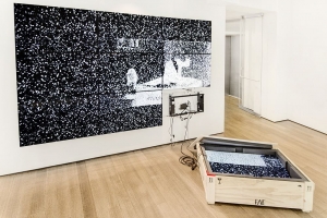 An image of Survivor's Remorse, a video installation with one flat-screen in a grid of 9 flatscreens on the ground in an open crate
