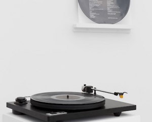 A photograph of A.K. Burns' record "Leave No Trace" installed on the wall in the background, and on a record player upon a pedestal in the foreground.