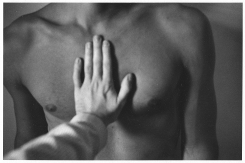 A black and white photograph of a hand on a man's chest.