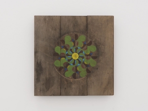 A pinwheel shape painted in green and purple on a square panel of wood
