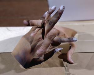 An image of fingers intermingled on a brown paper surface, made out of various collaged papers