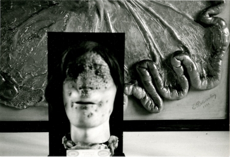 A black and white photograph of a wax figure with a burned face juxtaposed over an abstract, partial sculpture/diorama of body parts.