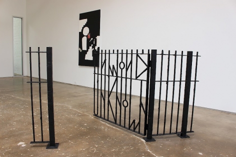 A photograph of the installation at SITE 131 that includes an A.K. Burns fence (Known Unknown) and a black-and-white Sadie Benning mixed-media work on the wall at right, behind the fence.
