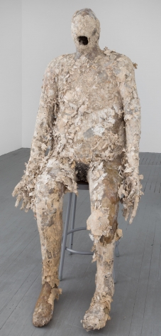 A sculpture of a nondescript sitting body, mouth open, hands by its side, with wisps of paper coming off of the body.