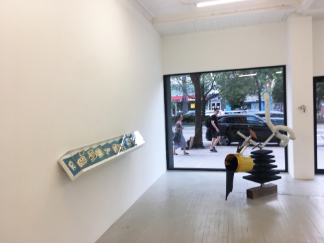 a photograph of the gallery with a sculpture on the ground and a leporello installed on the wall
