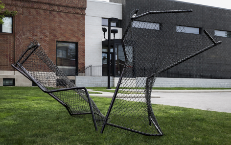 Black chain link fence sculpture jutting out of grass