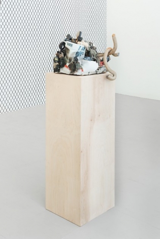 A ceramic sculpture on a raw wood pedestal, with the chainlink fence wallpaper in the background.