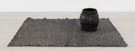 a black glazed vessel upon a woven rug