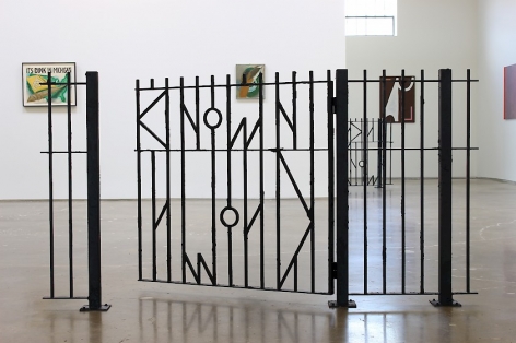 A photograph of the installation at SITE 131 with A.K. Burns' fence in the foreground, and several other works installed on the wall behind it, nearly illegible.