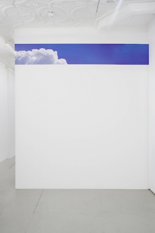 A swatch of vinyl with a photoshopped image of clouds on a blue sky, installed in a single line near the top of a wall in the back office of the gallery