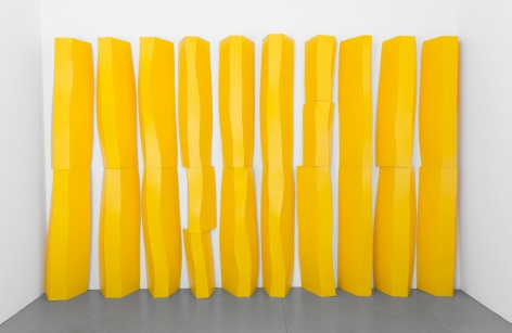 Organic shapes made from yellow corrugated plastic, creating large, rock-like objects standing against a wall. 10 total columns made up of multiple parts.