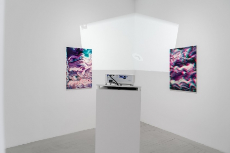 A straight-on view of 2 artworks situated around a corner in the gallery, with the back of the projector in the forefront. The light on the wall is a projection of the interior of the gallery via Google Maps.