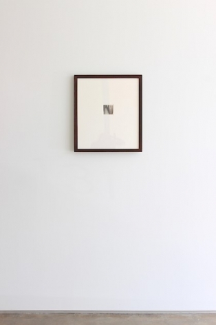 A photograph of the installation at SITE 131 of Lee Lozano's small graphite drawing in a black frame, hung on the wall.