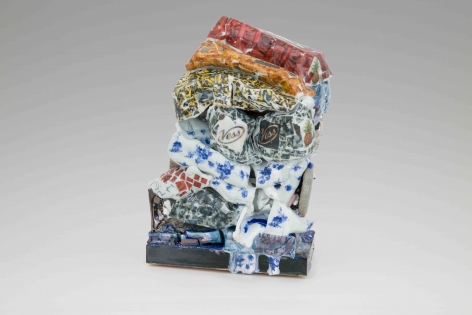 A sculpture of glazed and unglazed clay, stacked, with several different visible patters (cigarette images, blue flowers, red roses, orange fried chicken)