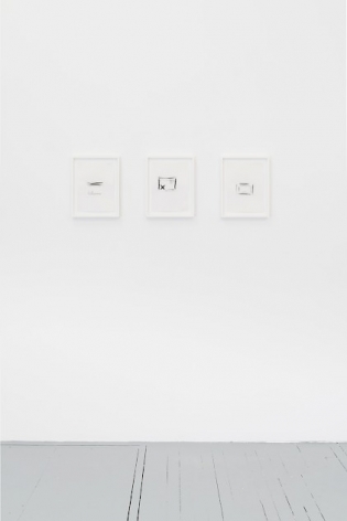 A photograph of three black and white drawings, framed in white, installed on the wall in a single row.