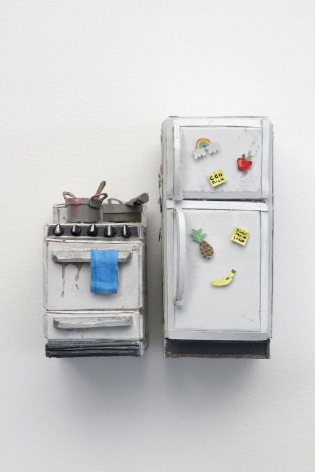 A stove with two dirty pots upon it and a closed refrigerator, crafted from paper and foam. The two items are next to each other with a small space between them, hung on the wall. The fridge has magnets on the exterior, and the stove has a towel hanging on the handle.