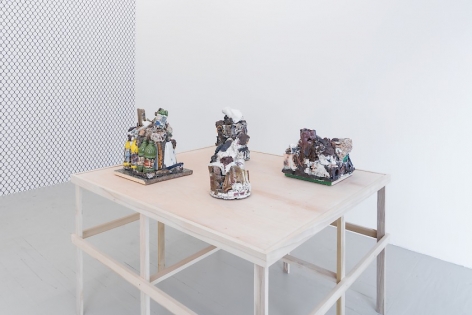 A photograph of a raw wood platform holding 4 ceramic sculptures. At left we see an excerpt of the gallery's temporary wall, upon which is mounted a chainlink fence wallpaper.