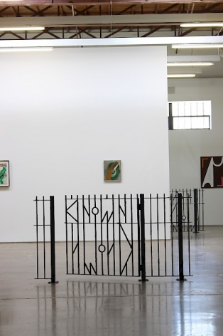 A photograph of the installation at SITE 131, including A.K. Burns' fence in the center and excerpts of 3 artworks installed on the wall in the background.