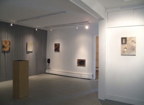 A photograph of the room: 2 works on a gray back wall with a wooden pedestal at left. There are 2 works on the far wall, and a work closer on the right wall