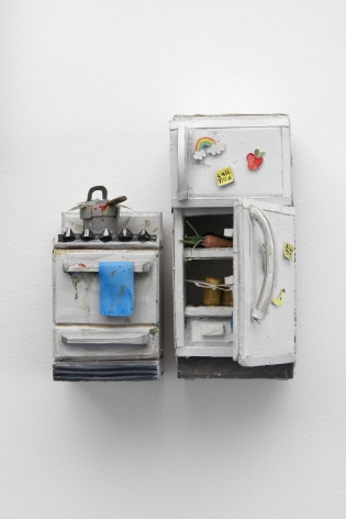 A stove with a dirty pot upon it and a refrigerator that is open, crafted from paper and foam. The two items are next to each other with a small space between them, hung on the wall. The open fridge has items within it (a carrot, a brown object) and magnets on the exterior.