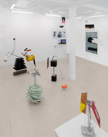 An installation view showing a cluster of 4 sculptures and two walls with drawings hung in a column